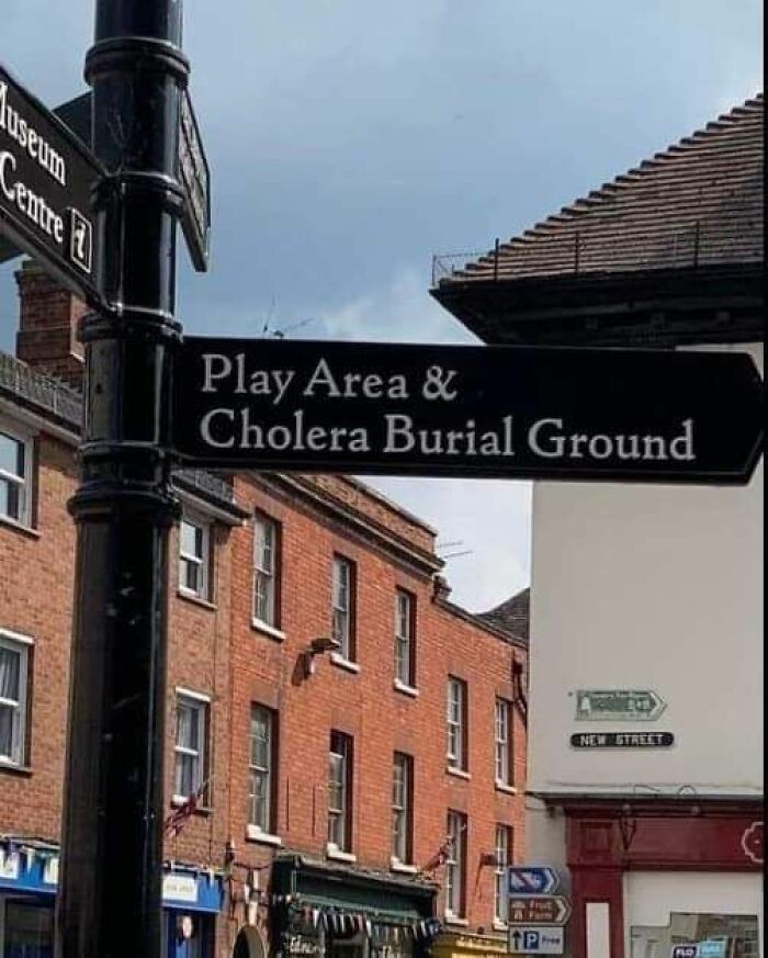 A street sign pointing to a "Play Area & Cholera Burial Ground" creating random memes or humor.