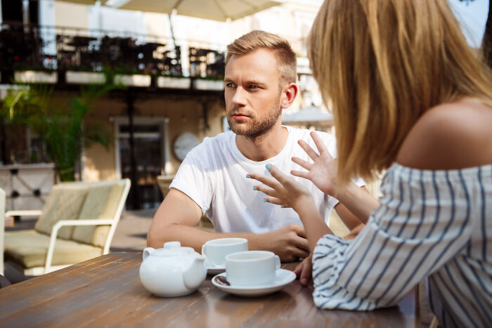 Man in a white shirt listening intently to a woman talking animatedly. Confidence and intelligence are key.