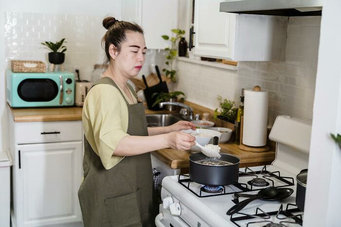 Woman cooking in kitchen adding rice to pot on stove