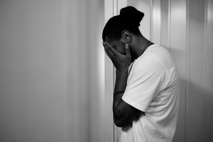 Man covering face in distress against plain wall, illustrating sharp comebacks to sexist men
