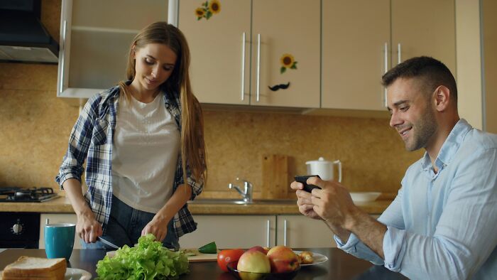 Woman chopping vegetables while man uses phone in kitchen