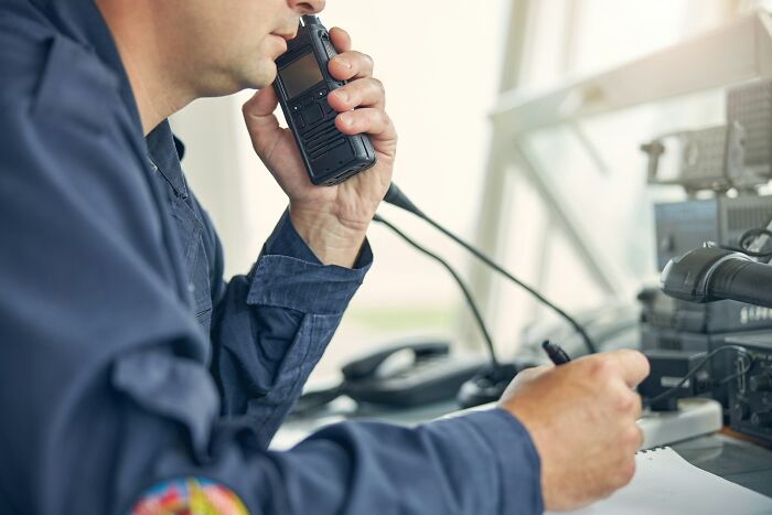 A person in a blue uniform speaks into a walkie-talkie, taking notes. Disturbing d***h stories often involve communication.
