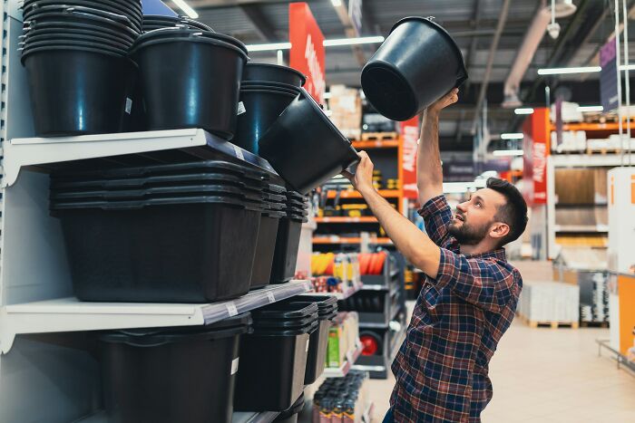 Man selecting a large black bucket in a home improvement store