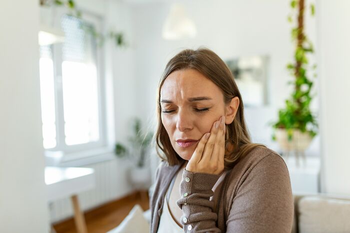 Woman clutching her jaw in pain, symbolizing health warning signs and the need for routine cancer screening.