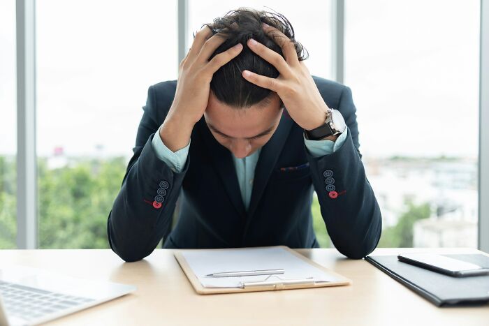 A stressed lawyer with hands on his head, looking down at paperwork, grappling with seemingly impossible cases.