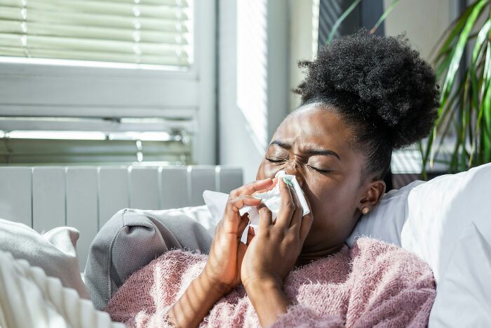 Sick woman blowing nose while resting on couch