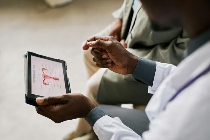A doctor discusses science facts, showing a female reproductive system on a tablet to a patient.
