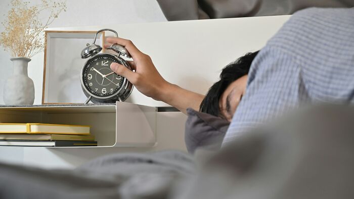 Person reaching to turn off analog alarm clock while lying in bed