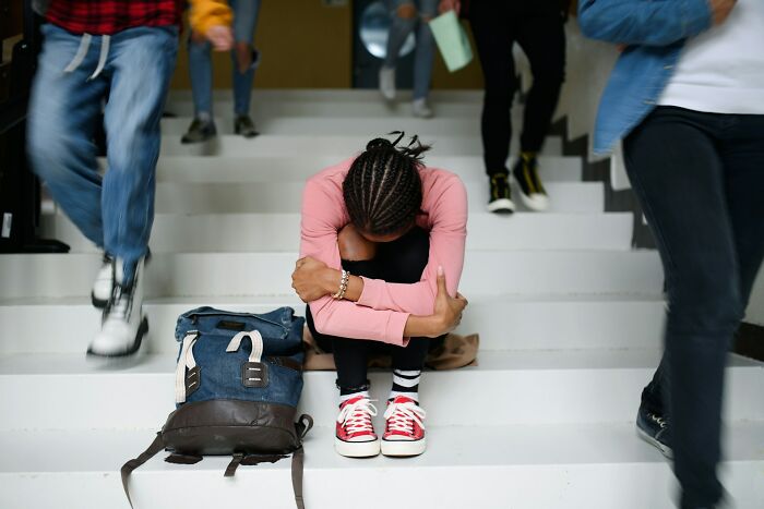 Sad student sitting on stairs with head down and backpack nearby