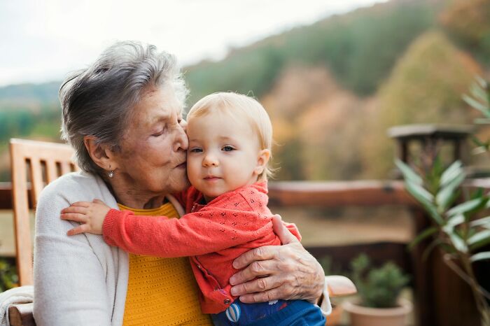 Grandmother kissing and hugging toddler outdoors with autumn trees