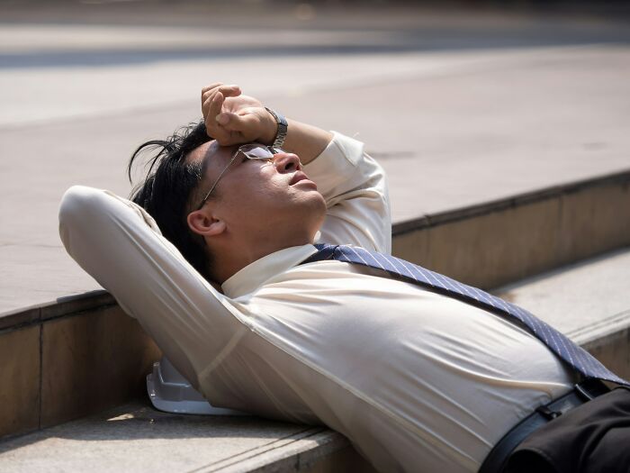 A man in a shirt and tie, looking tired and resting on steps. Fatigue can be a warning sign for cancer screening.