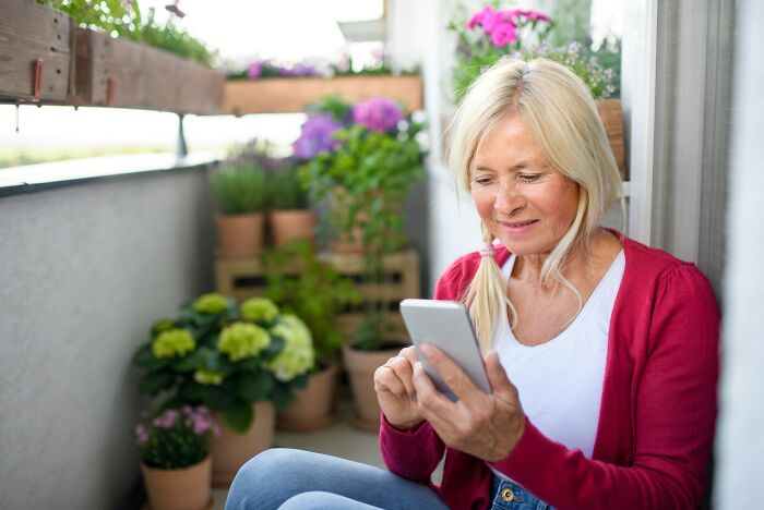 Blonde woman using smartphone on balcony with flowers