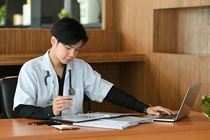 Doctor analyzing medical files and using laptop at desk