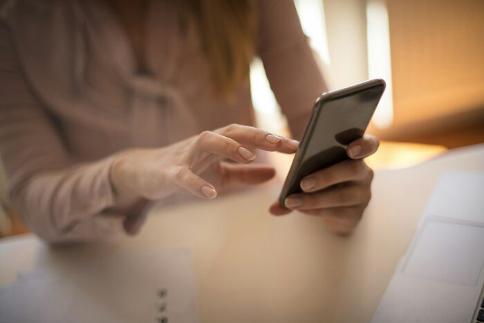 Mãos de uma mulher com unhas bem cuidadas batendo em um smartphone, representando o uso de uma balança inteligente para detectar trapaças.