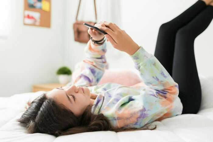 Young woman lying on bed using smartphone in casual clothes