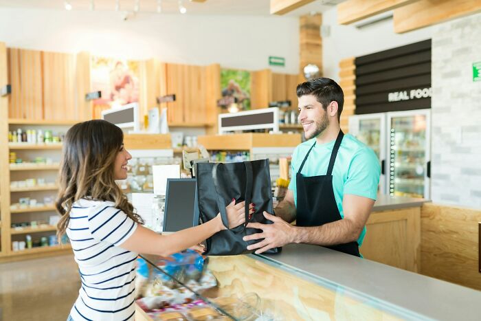 A smiling female customer receives a shopping bag from a cheerful male store employee, showcasing everyday silent luxuries.