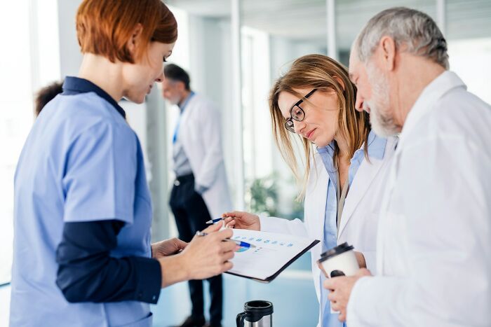Medical professionals, a nurse and two doctors, crossing to the other side to analyze a chart together with focus.