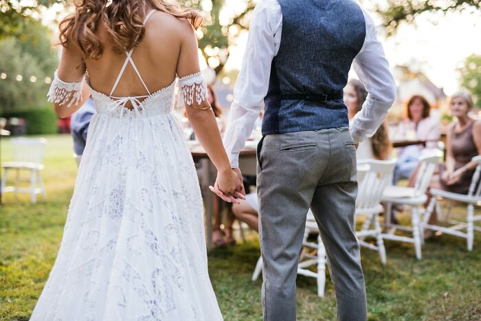 Back view of bride and groom holding hands at outdoor wedding ceremony
