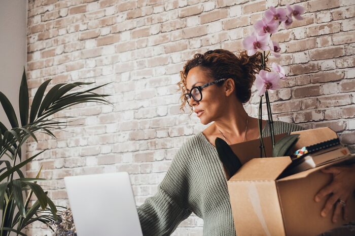 Woman packing boxes with plants at home laptop representing quitting over paycheck