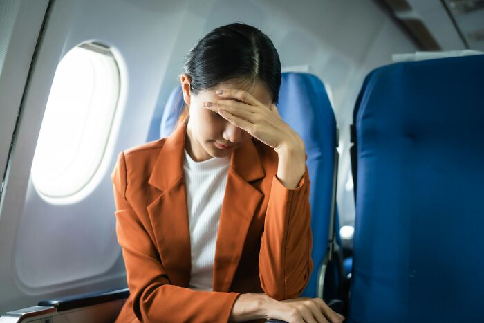 Woman on an airplane, looking distressed, holding her forehead. Highlighting the importance of routine cancer screening.