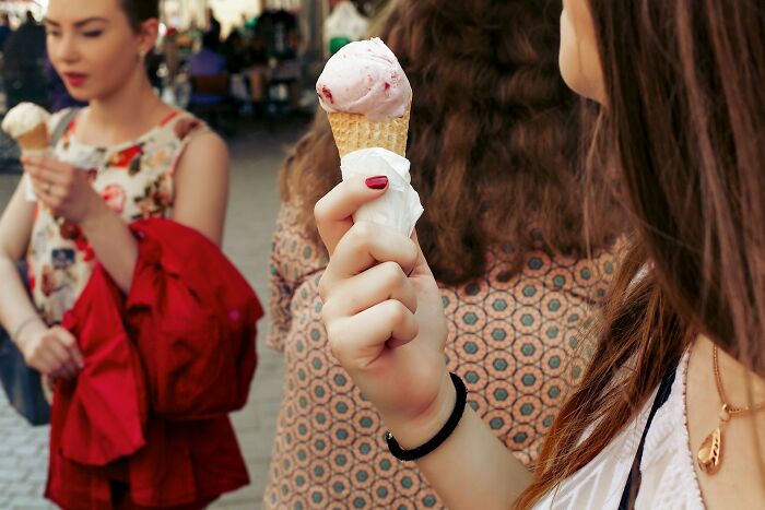 Two women enjoying ice cream outdoors. The foreground shows a hand holding a strawberry ice cream cone. Cool facts.