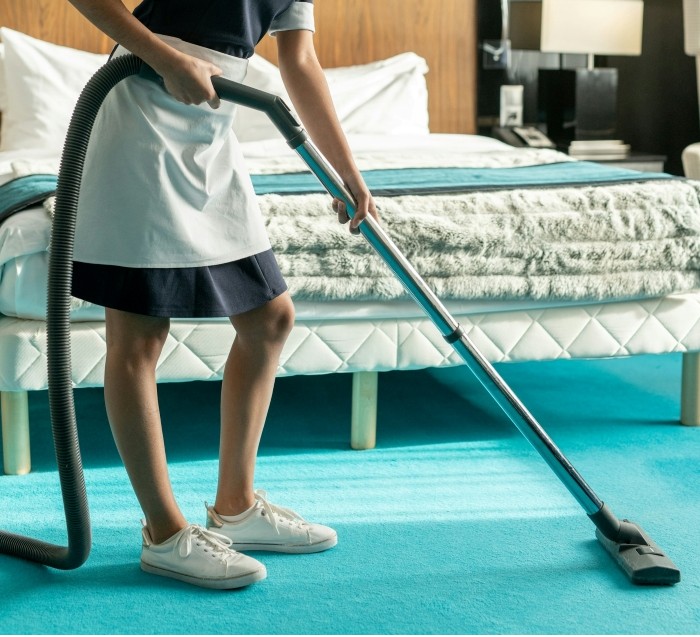 Hotel housekeeper vacuuming carpet near bed in guest room