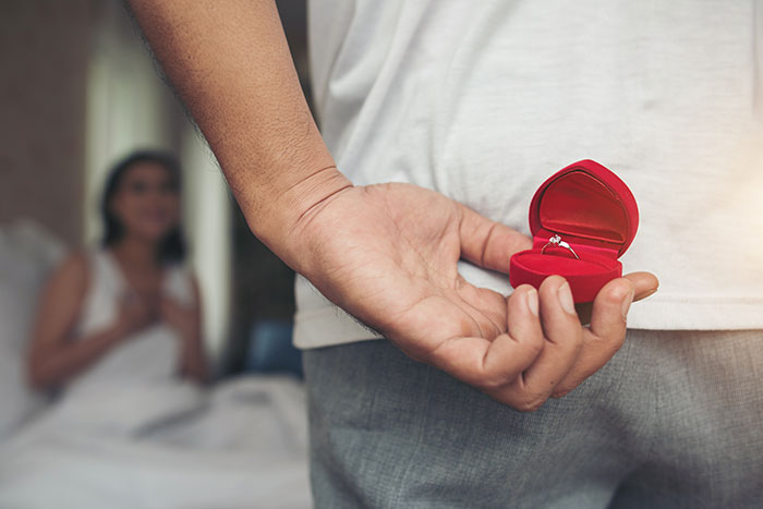 Man holding an engagement ring box behind his back Man holding an engagement ring box behind his back