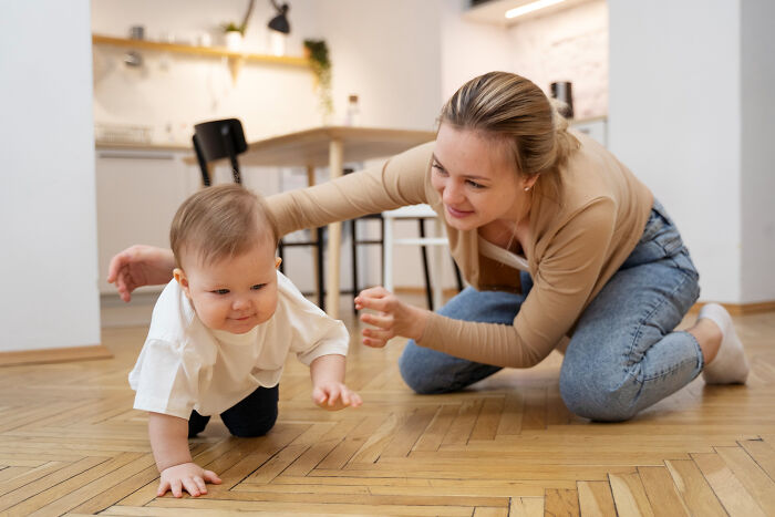 Mother encouraging baby crawling on wooden floor