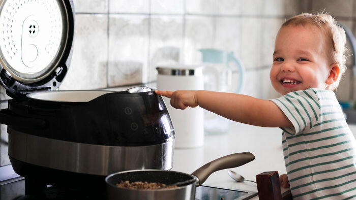 Smiling toddler touching open rice cooker in kitchen