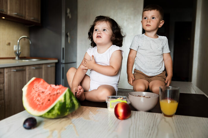Two kids sitting near watermelon with spilled juice