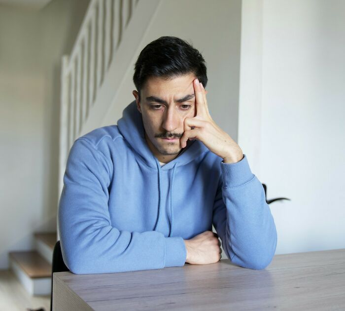 A man in a blue hoodie, looking pensive and concerned, resting his head on his hand. He represents men suffering.