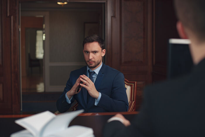 A serious lawyer in a blue suit, hands clasped, listening intently during a difficult case.