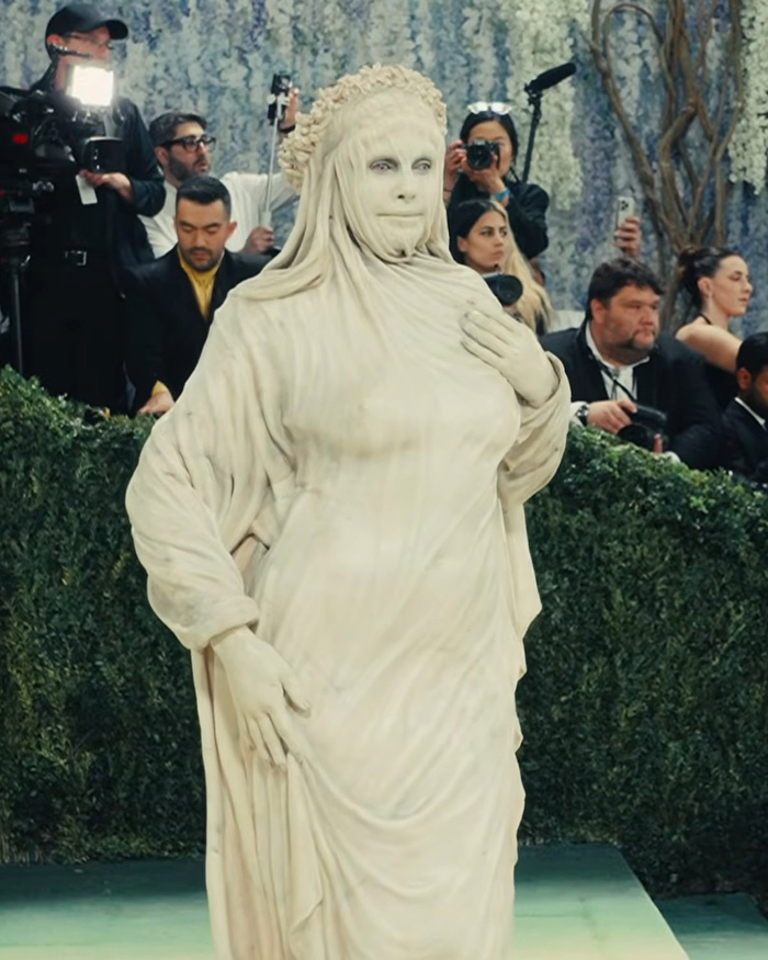 Heidi Klum's Met Gala outfit: a genuinely disturbing transformation resembling a draped statue, with onlookers in the background.
