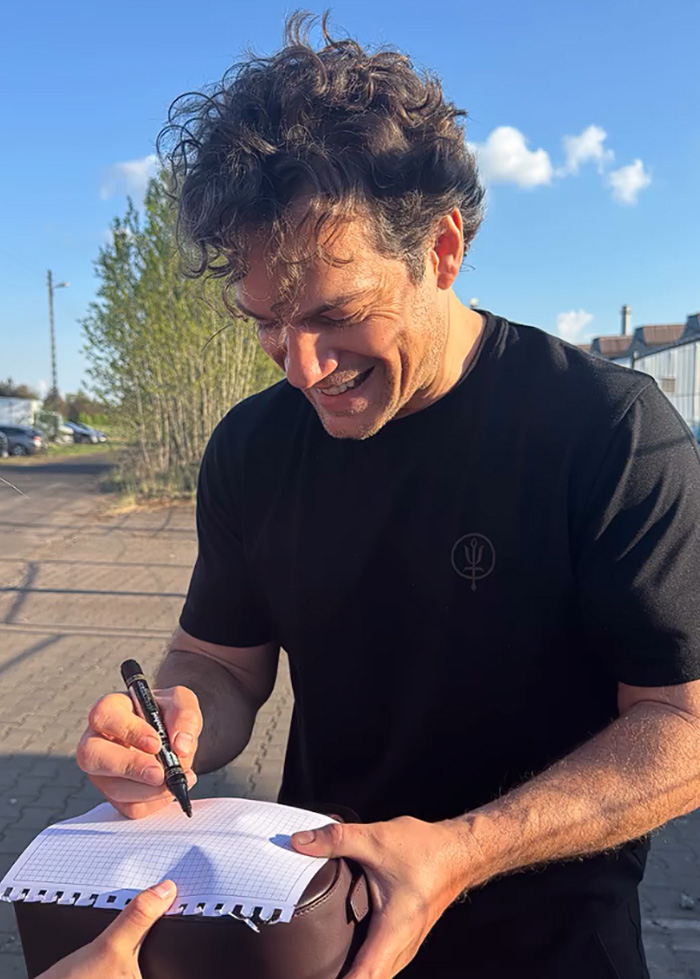 Man with curly hair smiling while signing autograph outdoors