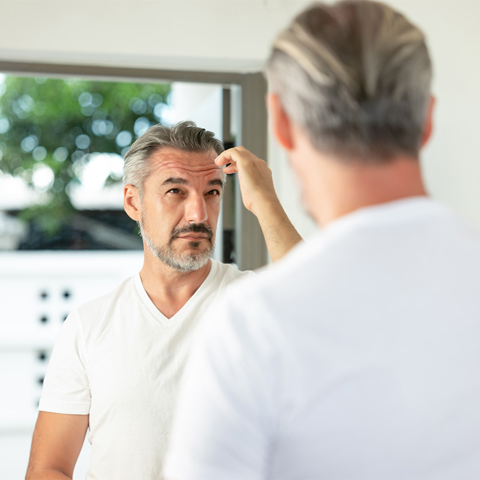 Middle-aged man checking hairline in mirror reflecting aging