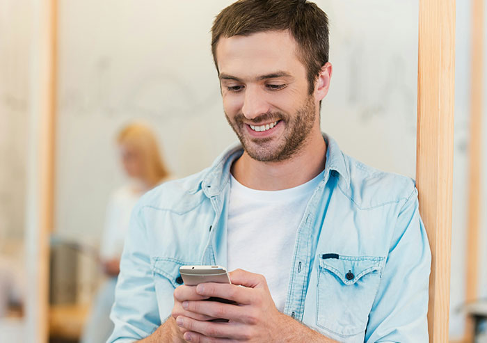 A smiling man in a denim shirt texts on his phone, recalling high school crushes.