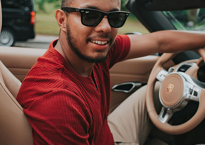 A smiling man in sunglasses and a red shirt driving a convertible. A high school crush could feel this confident.