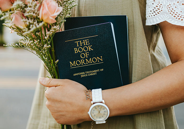 A person holding a bouquet of pink roses and a copy of The Book of Mormon. High school crushes often recall religious symbols.
