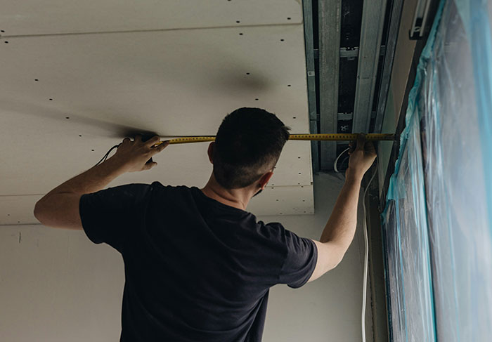 Person measuring ceiling indicating landlord property maintenance problems