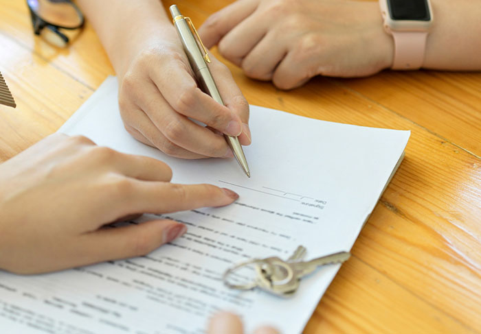 Hands signing rental agreement with keys on table for tenant lease