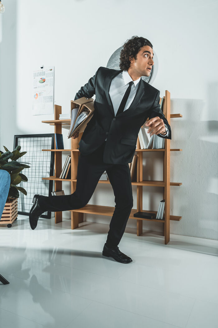 Man in business suit running with files in office quitting job