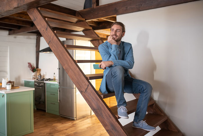 Man sitting on wooden stairs looking away, representing guy after bachelor trip Man sitting on wooden stairs looking away, representing guy after bachelor trip