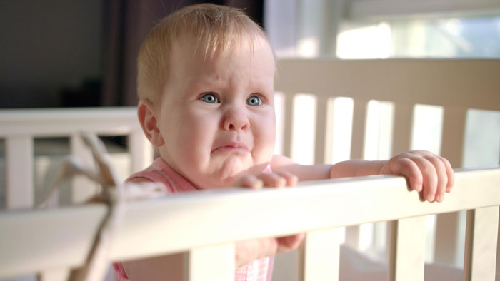 Crying baby in crib with concerned expression Crying baby in crib with concerned expression