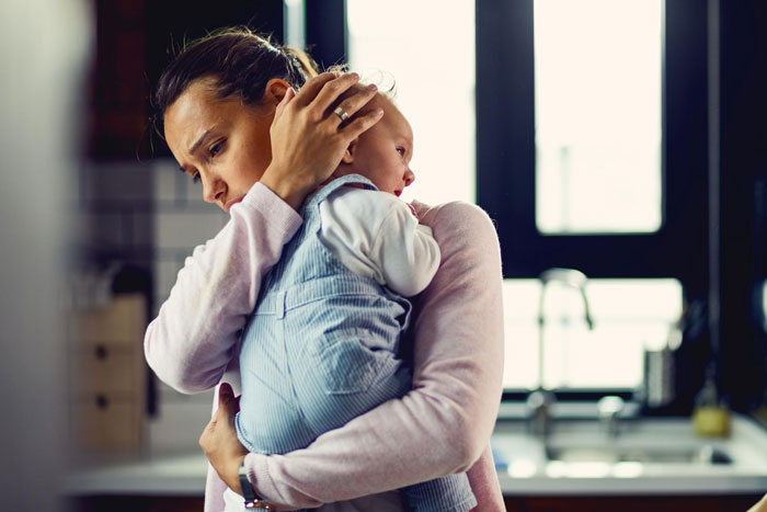 Worried mother holding sick baby at home during challenging parenting moment Worried mother holding sick baby at home during challenging parenting moment