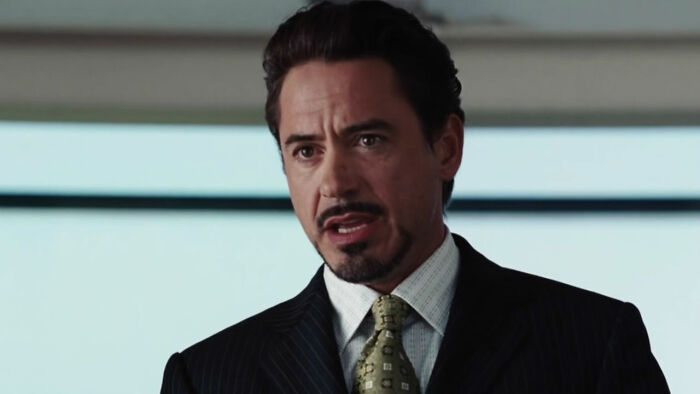 Robert Downey Jr. como Homem de Ferro, vestindo terno e gravata estampada, falando. Demolidor: disco Nascido de Novo.