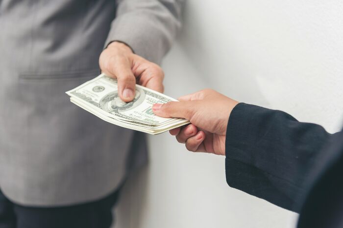 Hands exchanging US dollar bills, representing middle-class financial transactions and discussions around privilege.