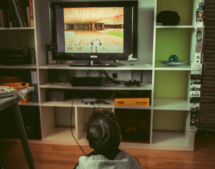 A child sitting on the floor watching a video game on a TV, reflecting themes of middle-class privilege.