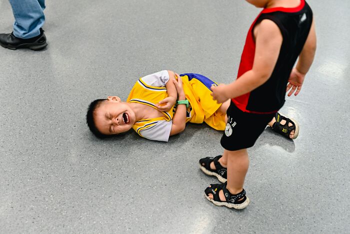 A child cries on the floor while another child stands nearby. This scene could expose privilege dynamics.