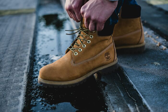 Hands tying brown work boots with yellow laces, standing in a shallow puddle. A relatable image for discussing privilege.