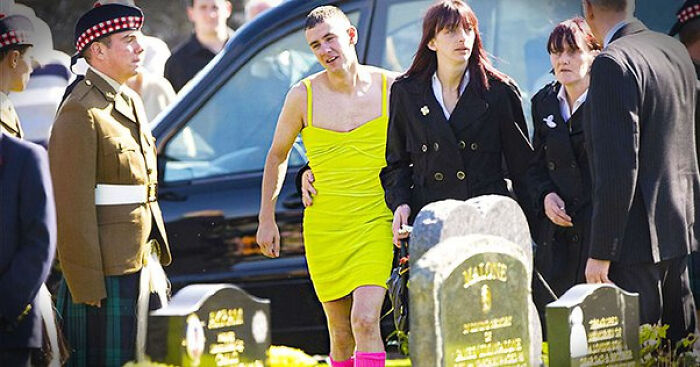 Man in bright yellow dress attends funeral with others near gravestones